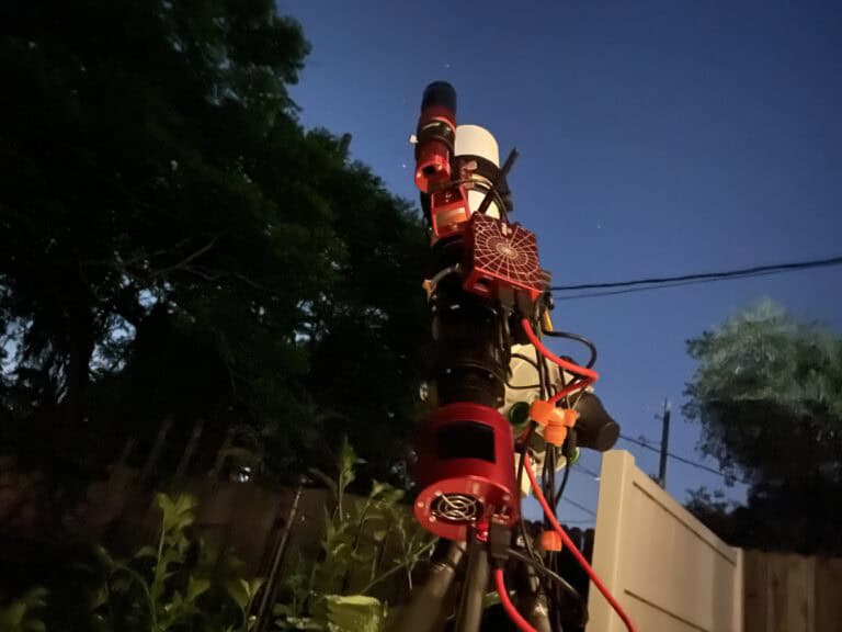 Astrophotography rig in a backyard pointed at open sky beside a tall tree line