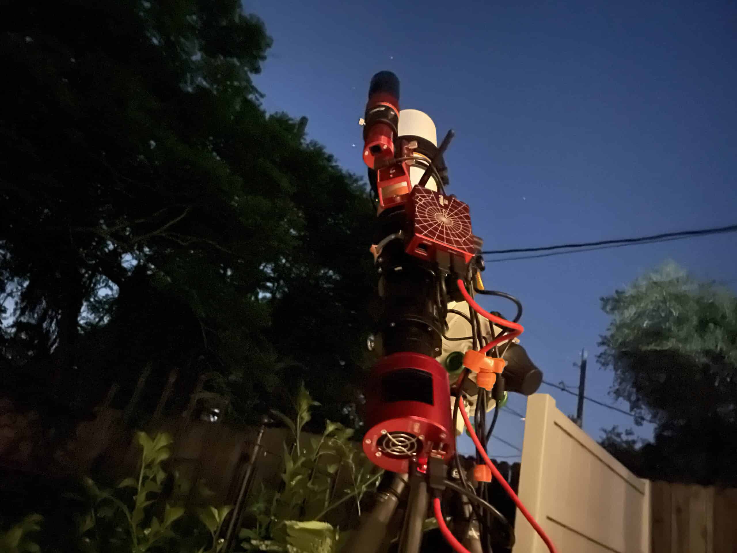 Astrophotography rig in a backyard pointed at open sky beside a tall tree line
